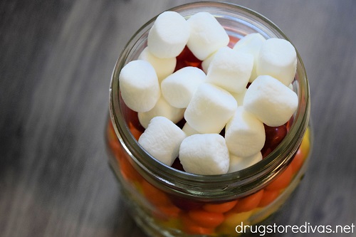 Mini marshmallows on the top of a mason jar that's filled with Skittles.