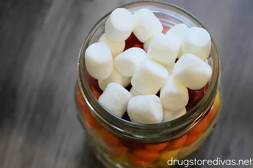 Mini marshmallows on the top of a mason jar that's filled with Skittles.
