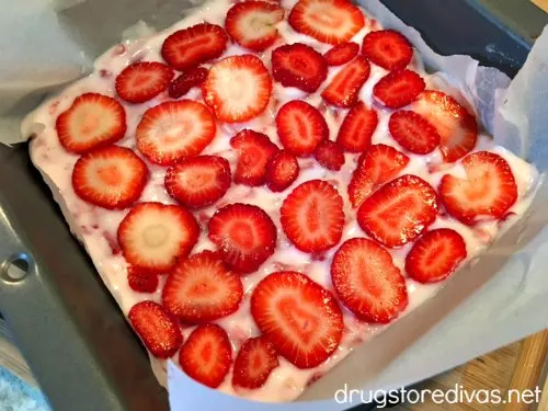 Sliced strawberries on top of yogurt in a pan with parchment paper.