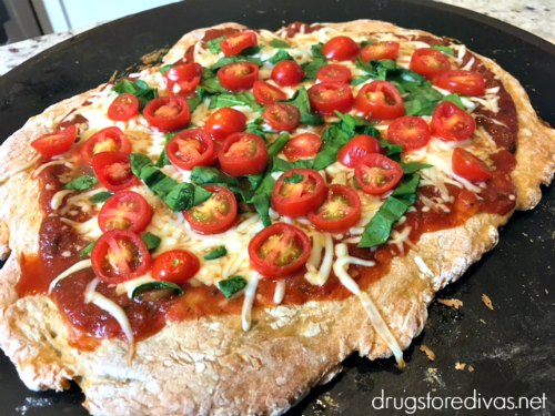 Pizza, topped with sauce, cheese, tomatoes, and basil, on a pizza stone.