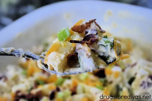 A spoon holding a scoop of loaded baked potato salad above a bowl of loaded baked potato salad.
