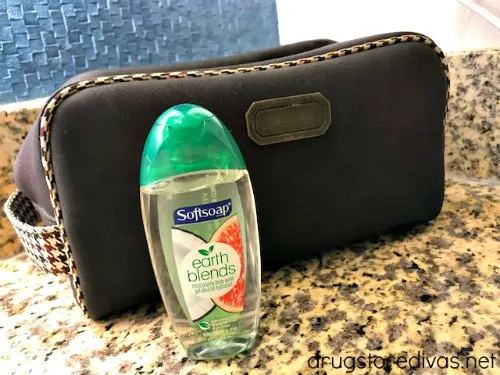 A trial size body wash in front of a black toiletry bag.