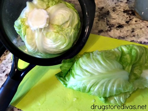 Cabbage in a strainer and cabbage leaves on a cutting board.