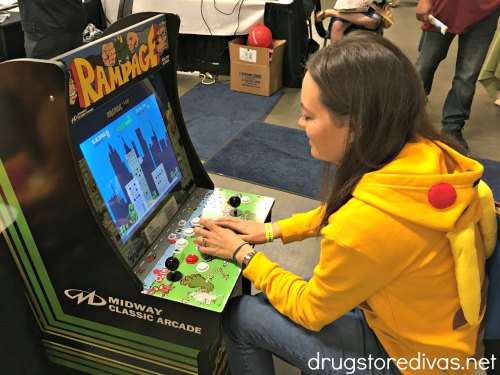 A girl in a Pikachu hoodie playing a Rampage video game.