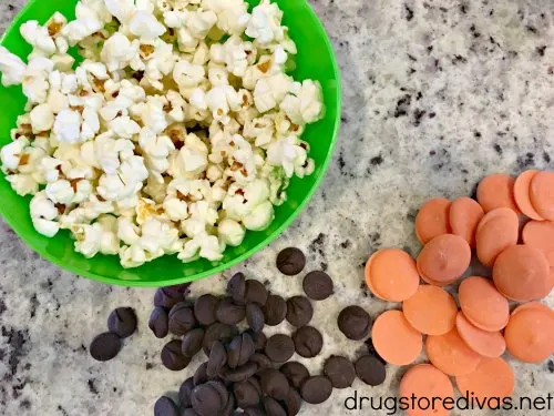 Popcorn in a bowl, chocolate chips, and orange candy melt.