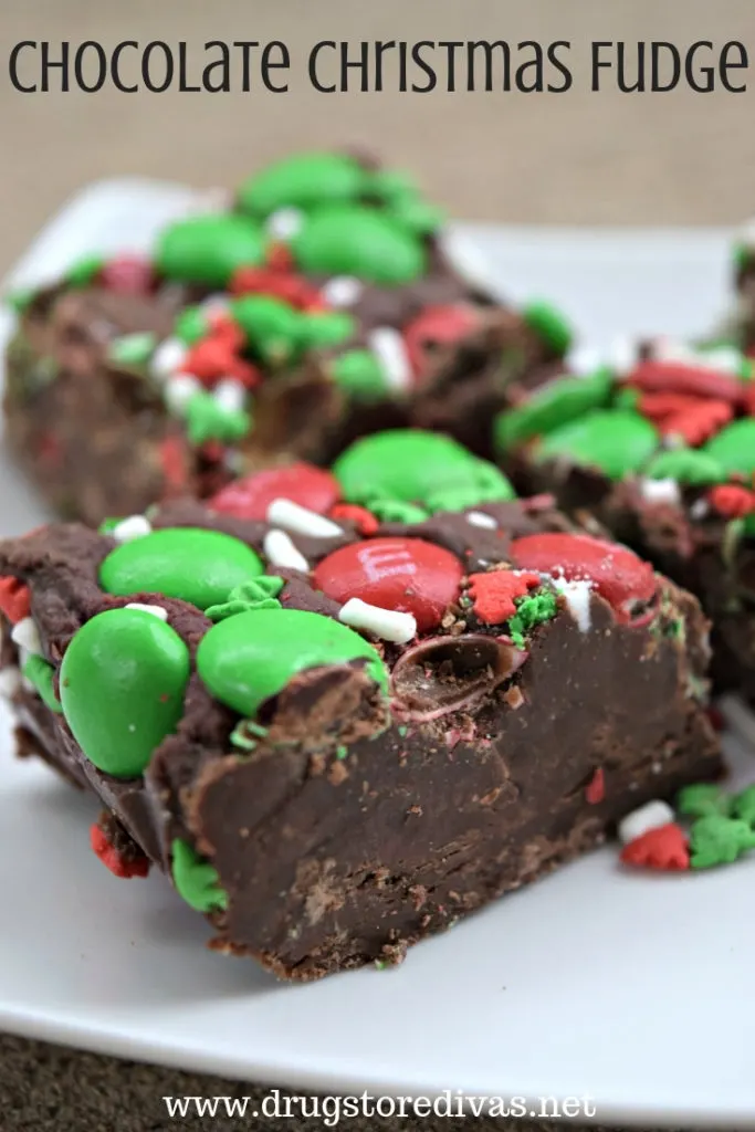 Pieces of chocolate fudge with red and green M&M candies and white sprinkles on top with the words "Chocolate Christmas Fudge" digitally written on top.