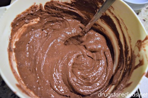 Chocolate cake mix in a white bowl with a spoon it in.