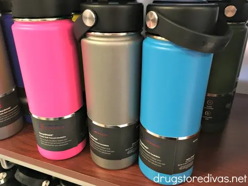 A pink, gray, and blue water bottle on a shelf, with others around them.