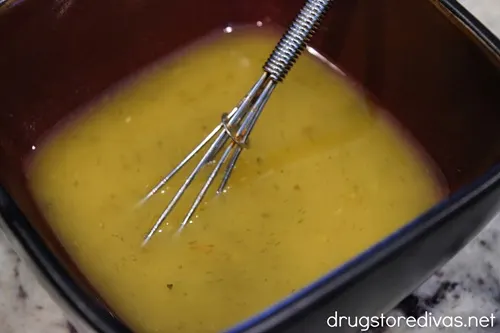 A vinaigrette dressing and a small whisk in a red bowl. 