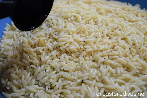Dressing being poured only cooked orzo in a blue bowl.