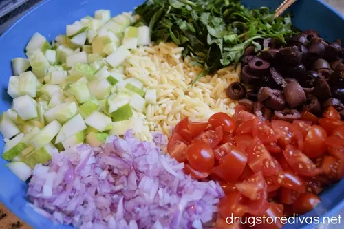 Chopped cucumber, red onion, cherry tomatoes, olives, and greens in a bowl with orzo.