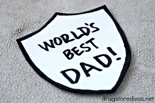 A shield made from a piece of white card stock with the words "World's Best Dad!" written on it.
