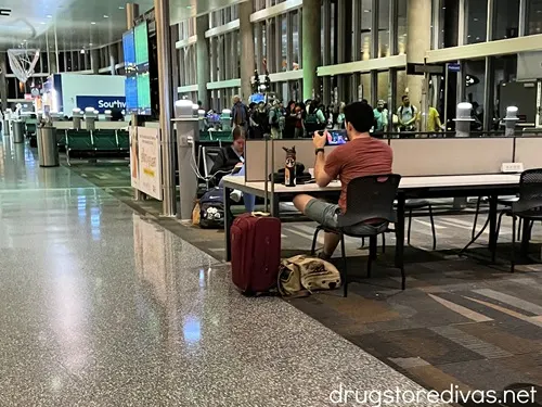 A man sitting at a table at an airport gate watching a show on a tablet.