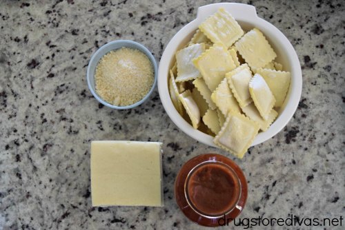 Ravioli, Parmesan cheese, mozzarella cheese, and marinara sauce on a counter.