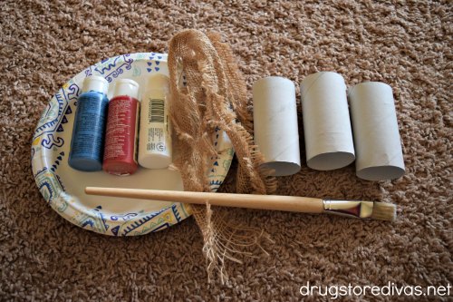 A paper plate, red, white and blue paint, a piece of burlap, a paint brush, and three toilet paper roll tubes.