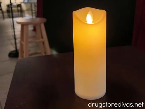 A flameless candle on a table in a dark room with a stool behind it.