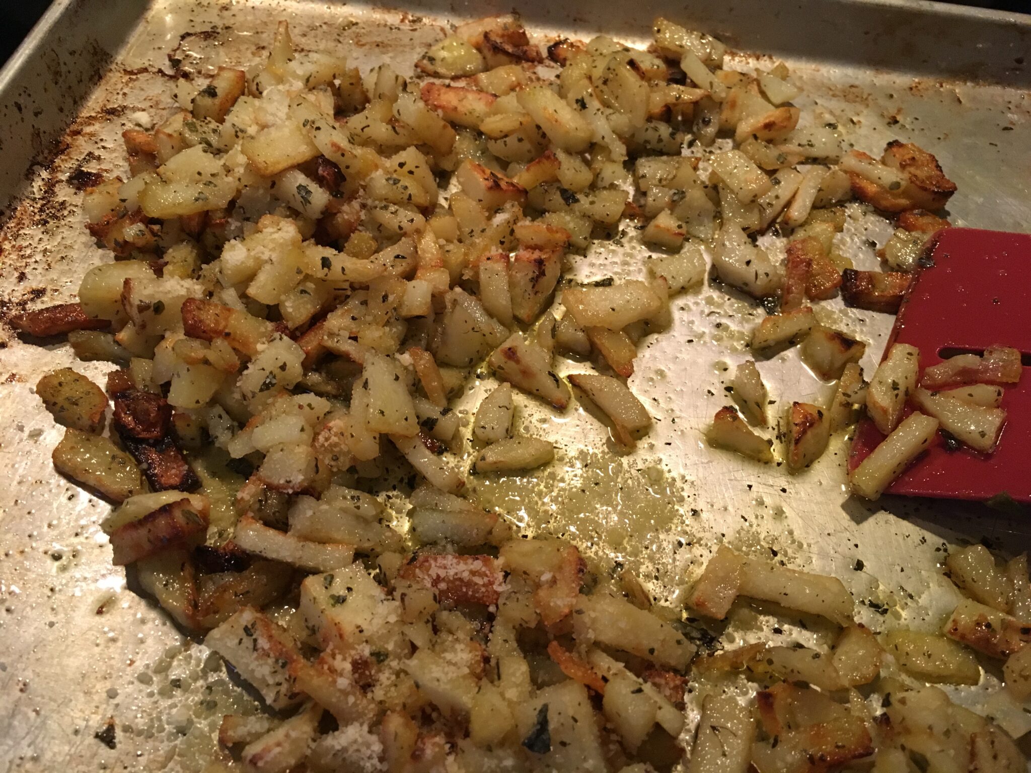 Cooked diced potatoes on a baking pan with a spatula.