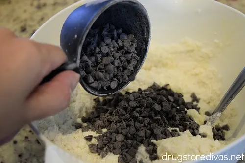 Chocolate chips being poured from a measuring cup into a bowl of white cake mix.