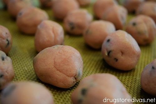 Pink cake balls with chocolate chips in them on a cookie sheet.