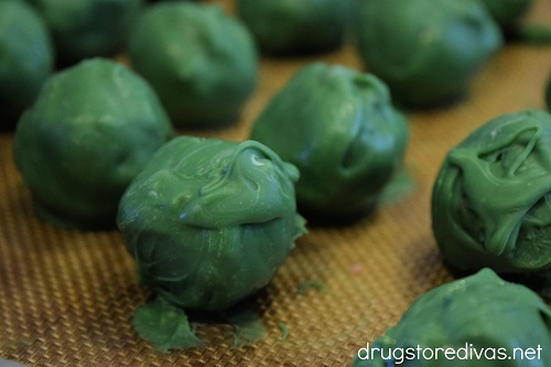 Green candy melt covered cake balls on a cookie sheet.