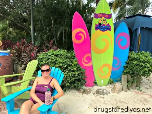 A woman sitting in a beach chair in front of three surfboards that say Aquatica.