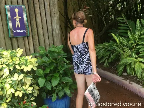 Woman walking into a restroom holding a wet bathing suit bag.