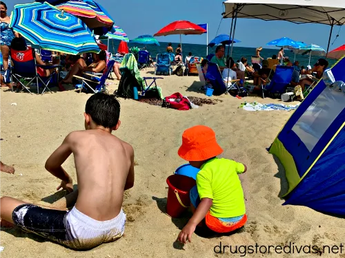 Two boys on the beach next to a beach tent.