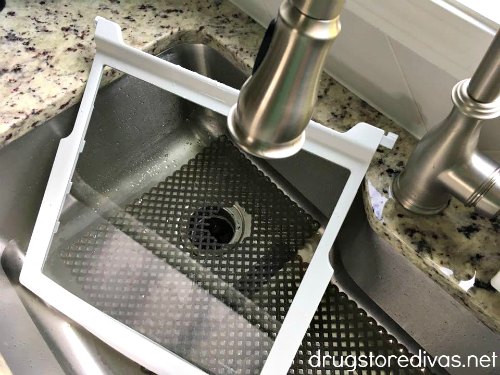 A fridge shelf being washed in a sink.