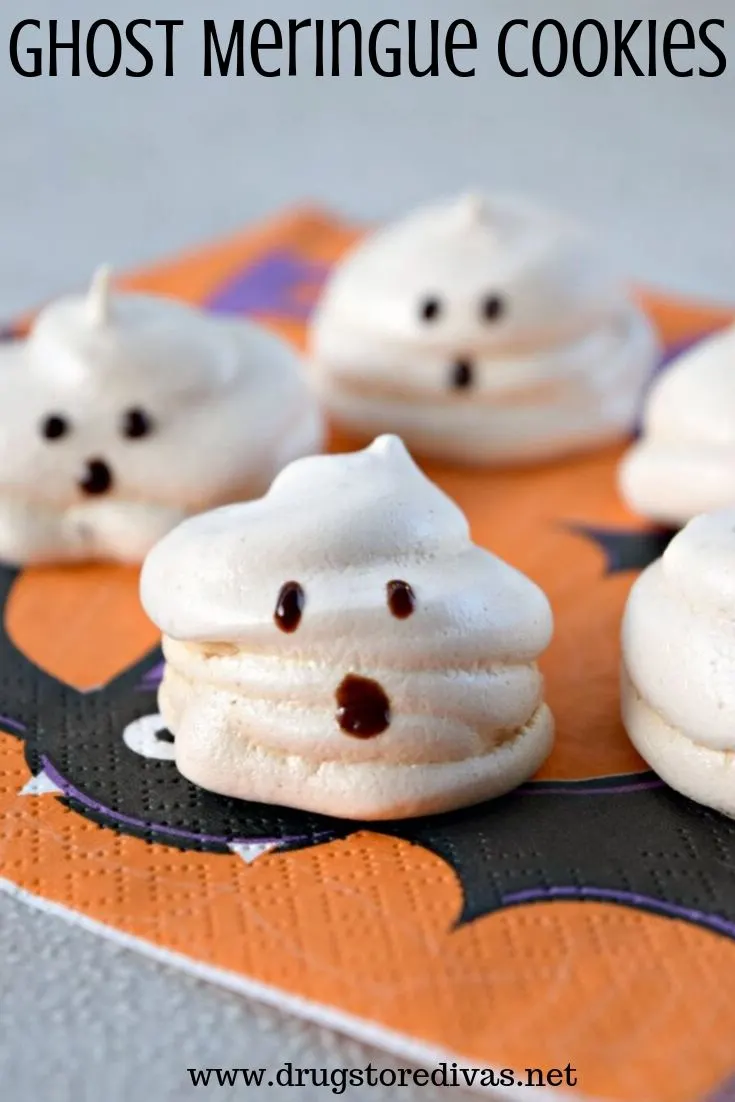 Ghost-shaped meringue cookies on an orange napkin with bats on it.