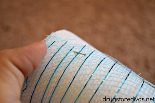 A hand holding a white foam cone with blue striped decorative mesh around it.