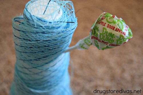 A green lollipop sticking out of a cone wrapped in blue decorative mesh.