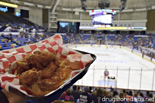 Fried chicken and waffles in a basket in the foreground with a hockey rink in the background