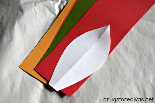 Four strips of colored card stock with a white piece, shaped like a feather, on top of them.
