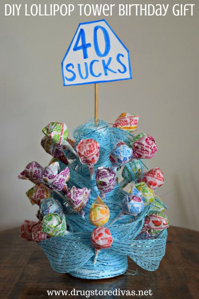A tower of lollipops with blue mesh wrapped around them and a "40 Sucks" tag out the top with the words "DIY Lollipop  Tower Birthday Gift" digitally written on top.