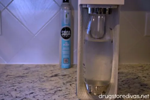 Soda maker on a counter in the foreground with a CO2 bottle in the background. The bottle says Soda Sense on it.