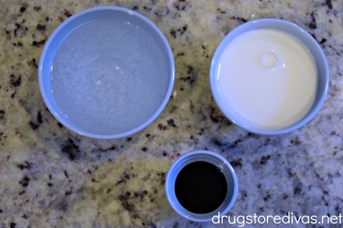 The small blue bowls on a counter. One has seltzer, one has milk, one has chocolate syrup.