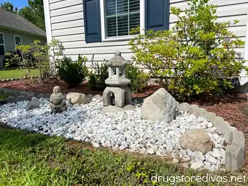 A Japanese rock garden, with a lantern and statue, in front of a home.