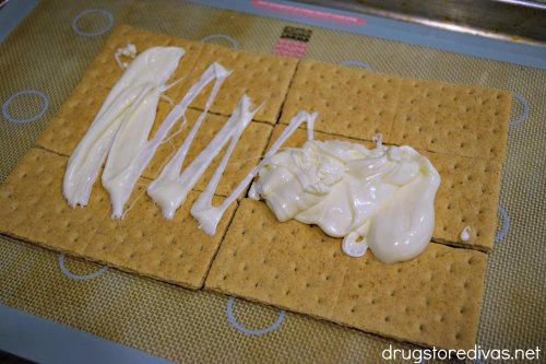 Graham crackers on a silicone baking mat with melted white chocolate on top.