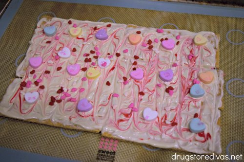 Conversation hearts and heart-shaped sprinkles in red and white chocolate on top of a silicone baking mat.