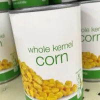 Cans of corn on a shelf in a store with the words 