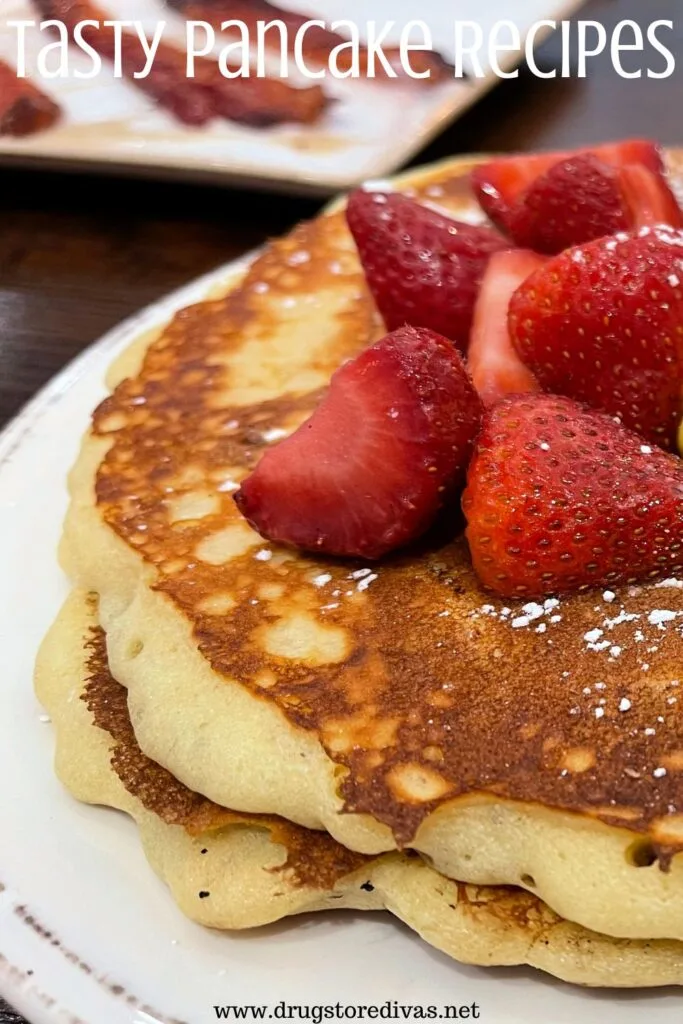 Two pancakes with strawberries on top on a white plate with a plate of bacon behind them and the words "Tasty Pancake Recipes" digitally written on top.