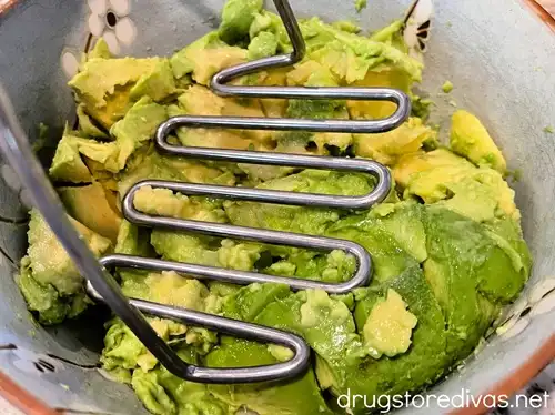 A potato masher in a blue bowl, mashing avocado.