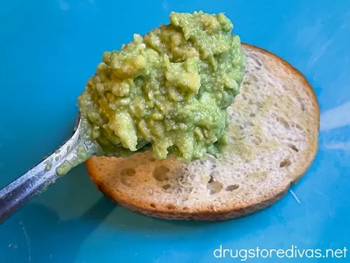 A spoonful of avocado mash above a piece of small toast on a blue tray.