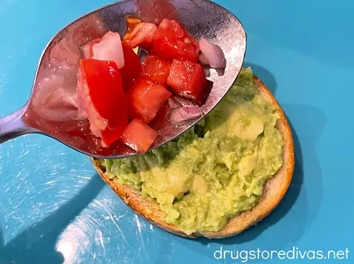 A spoonful of diced tomato above a piece of small toast with mashed avocado on it on a blue tray.