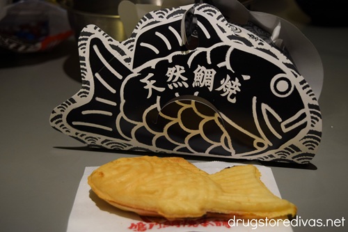 A fish-shaped pastry, called taiyaki, in front of a black fish-shaped package on a table.