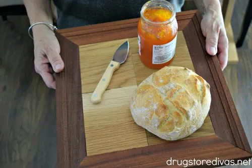 A woman holding a homemade serving tray with a knife, jelly, and bread on it.