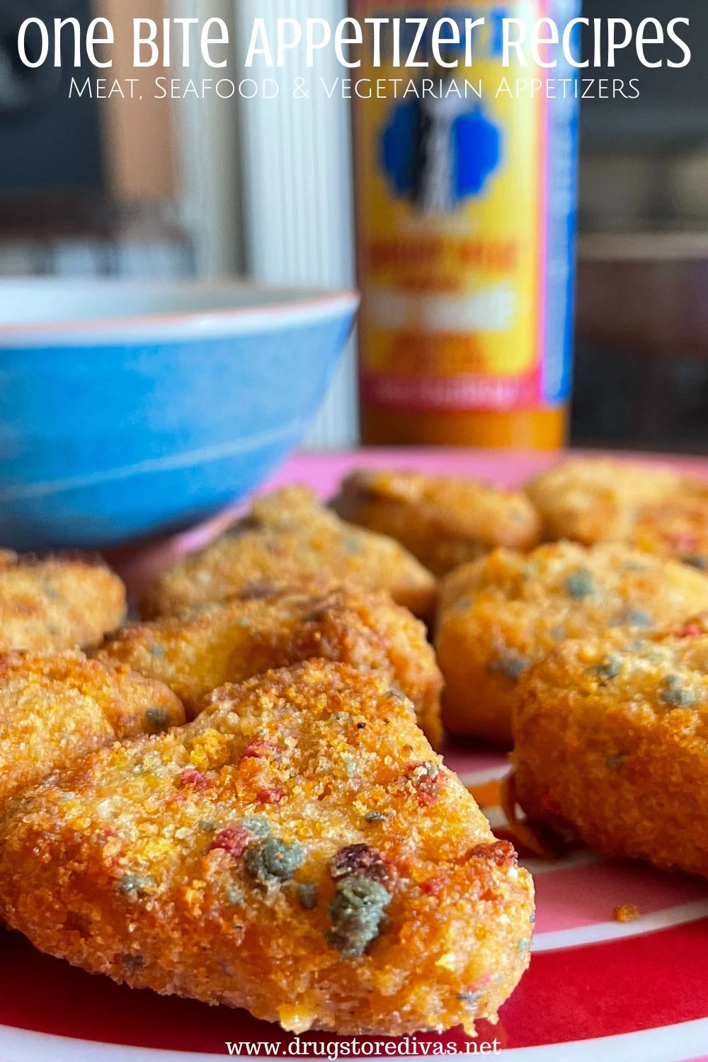 Fried triangle bites on a red plate with a blue bowl in the back and a bottle of sauce behind it with the words 