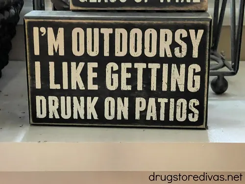 A black sign with white letters that says "I'm outdoorsy I like getting drunk on patios".