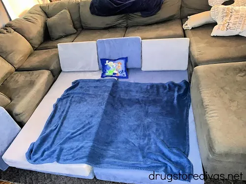 A Nugget couch with a blanket and pillow on the floor.