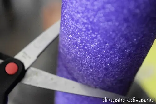 Scissors cutting a purple pool noodle.